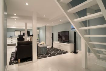 Modern open-concept living room with staircase, black sofa, TV console, and patterned rug in a bright home