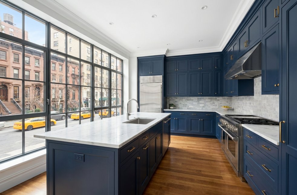 Modern Manhattan apartment kitchen with navy cabinets, marble island, and large city-view windows